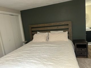 Neatly made bed with white bedding and pillows in a bedroom with a dark green accent wall